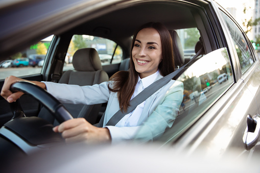 Portrait of cute female driver steering car with safety belt